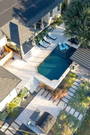 Aerial view of a modern backyard with a rectangular pool, lounge chairs, patio seating, landscaped greenery, and stone pathways.