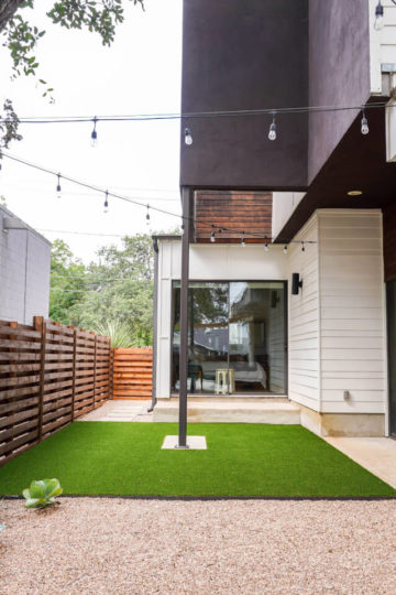 A small backyard with a mix of grass and gravel enclosed by a wooden fence.