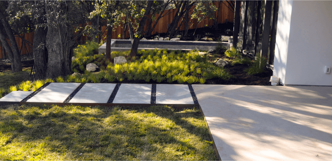 Smooth rectangular pavers laid out evenly leading to a concrete area in front of a house.
