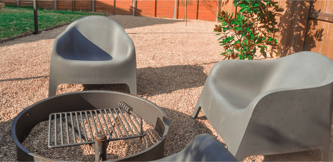 2 gray chairs on gravel surrounding a small grill.