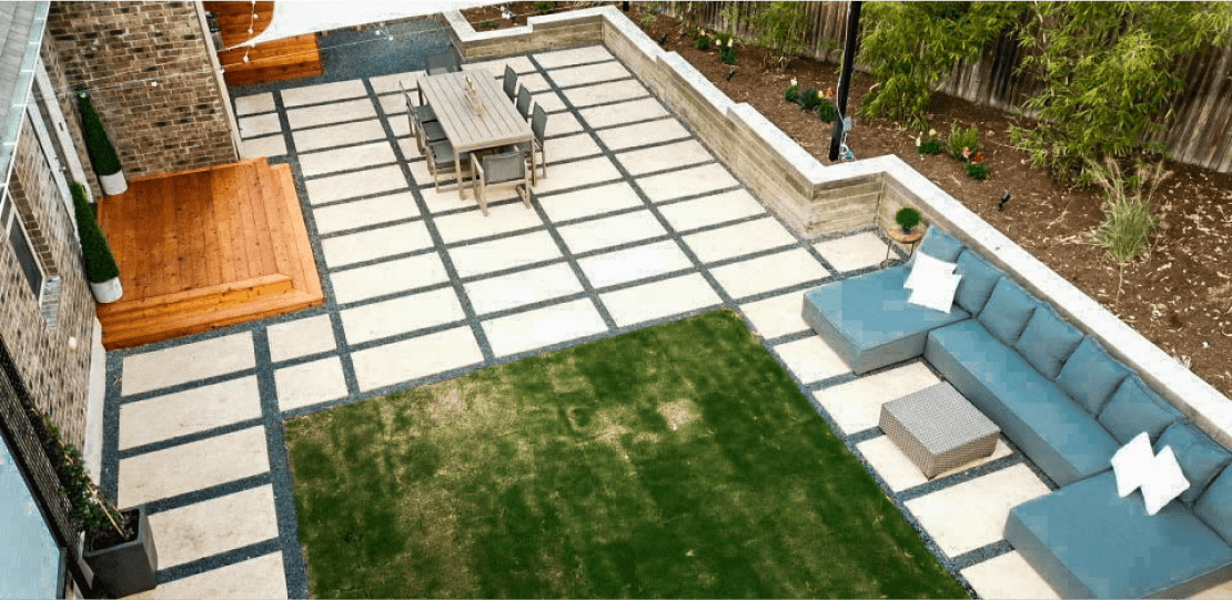 Birdseye view of a hardscaping and grass backyard. It is furnished with a blue sectional sofa, dining table, and awning.