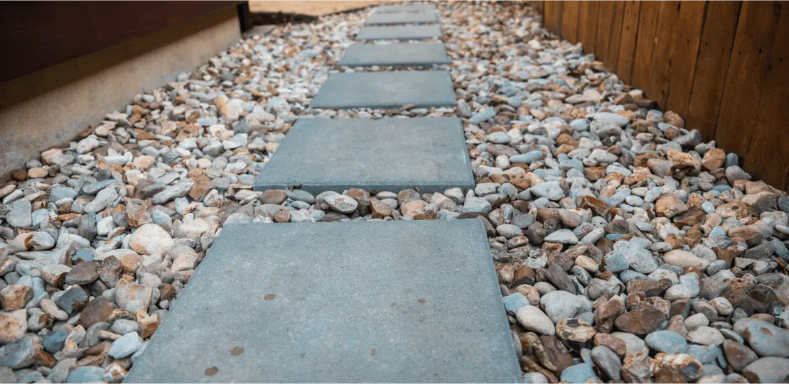 Square pavers in a row surrounded by small stones.