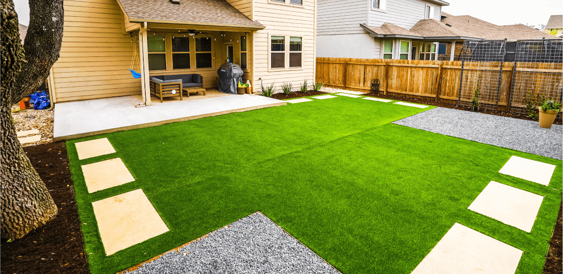 A mostly empty grassy backyard. Rectangular paved stones line the edges of the grass.