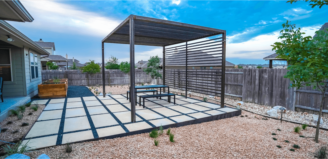 A backyard with a metal pergola on hardscaping tiles surrounded by gravel.