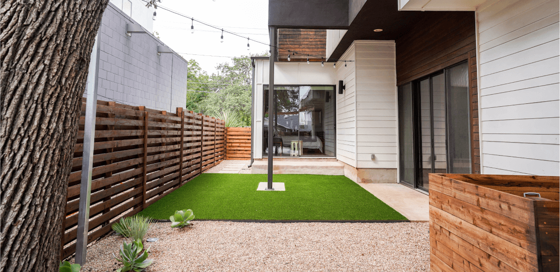 A small backyard with a mix of grass and gravel enclosed by a wooden fence.
