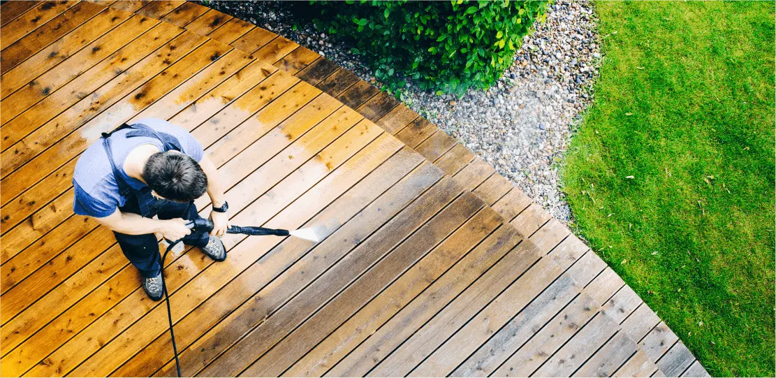 A person power washing a wooden deck.