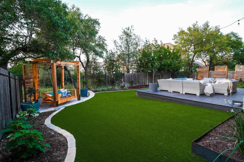 A backyard with grass, gray sofas, and a wooden swing.