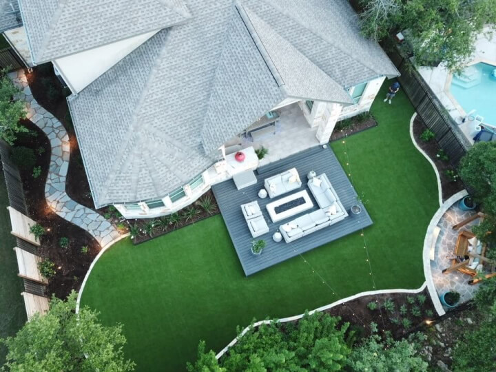 A birdseye view of a backyard patio furnished with chairs, sofas, and a fire pit surrounded by grass.