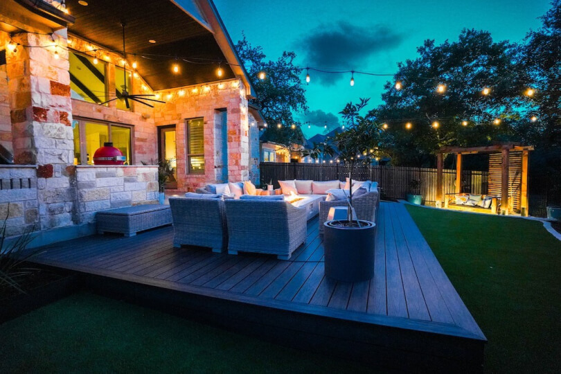 Raised wooden patio area with outdoor sofas and chairs underneath string lights.