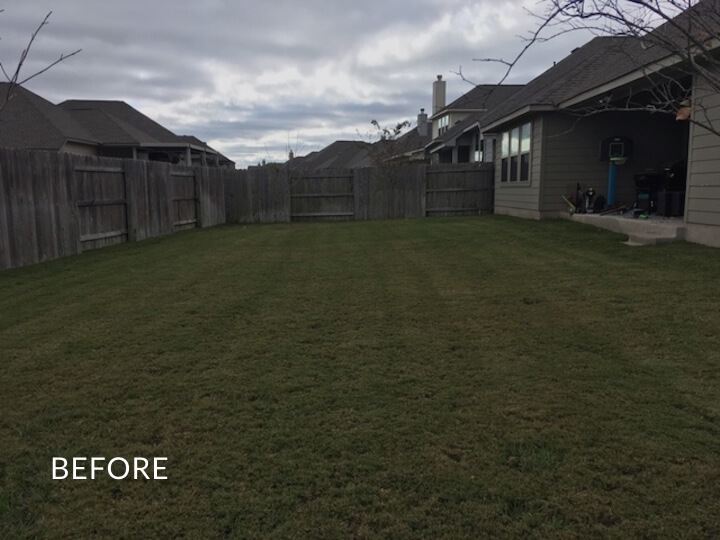 An empty backyard of grass enclosed by a basic wooden fence with the word 'before' overtop the photo.