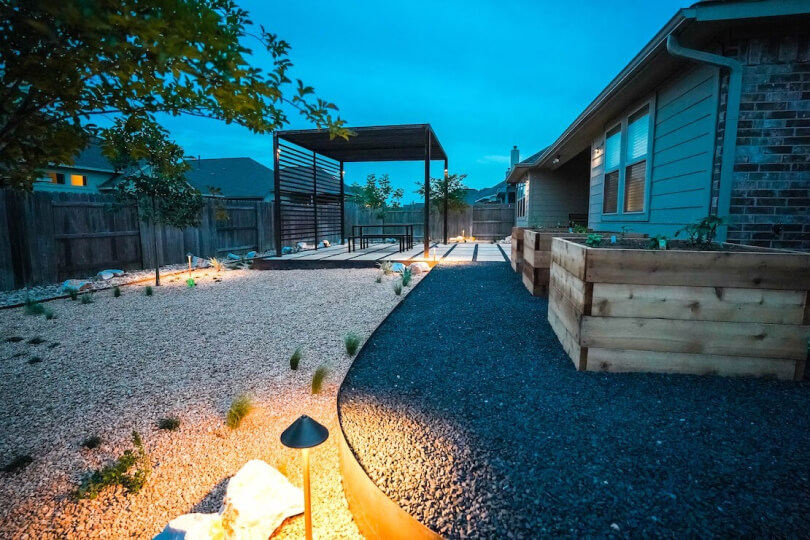 Side view of backyard with separated gravel sections and a small flood light.