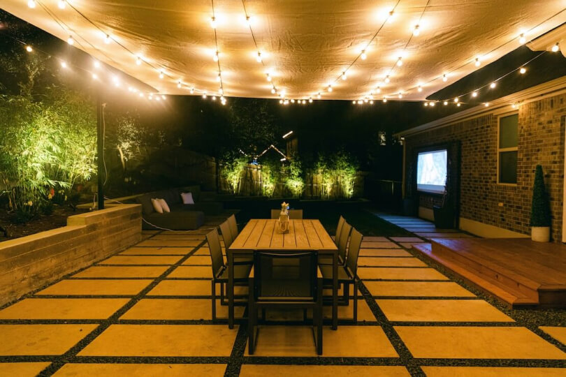 Hardscaping tiles in a backyard shown at night with string lights illuminating the space.