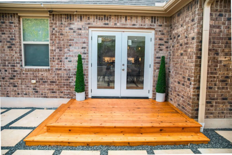 A glossy wooden landing outside a white double door back entrance to a house.