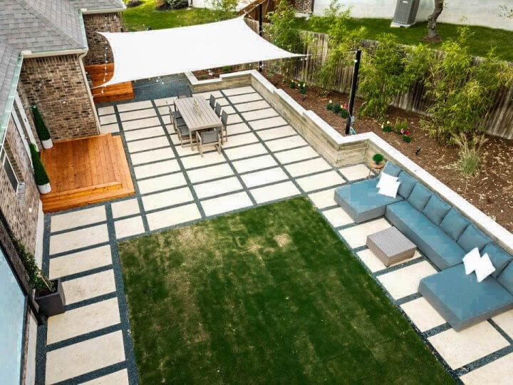 Birdseye view of a hardscaping and grass backyard. It is furnished with a blue sectional sofa, dining table, and awning.