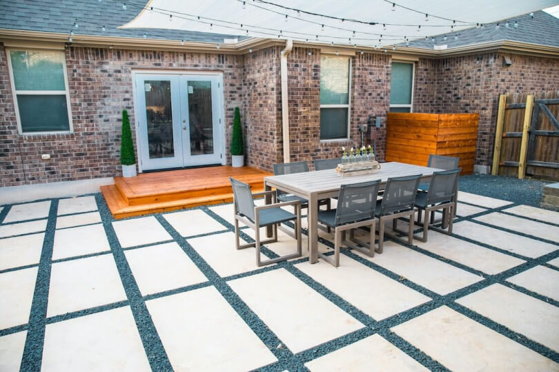 Backyard hardscaping of rectangular tiles with gravel in between shown with a table and 8 chairs atop it.