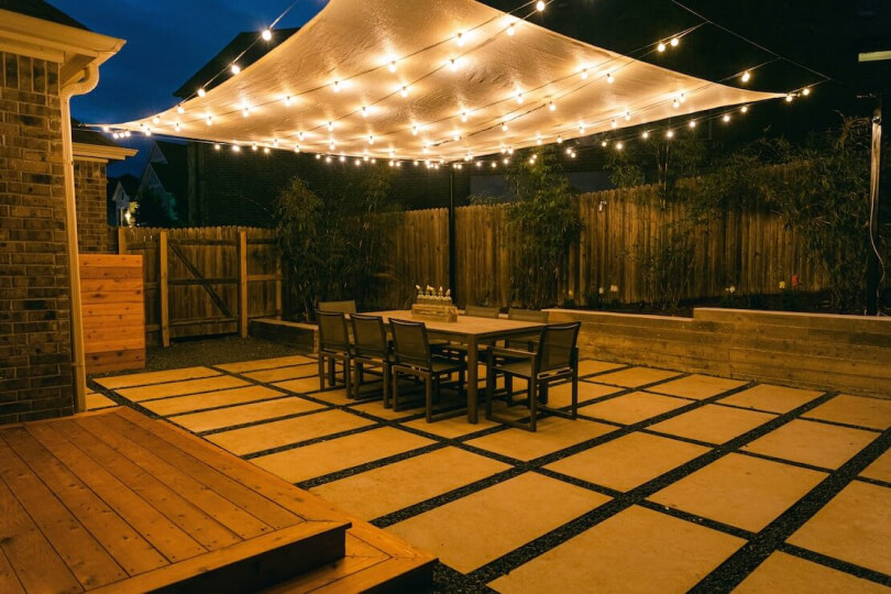 Hardscaping tiles in a backyard shown at night with string lights illuminating the space.