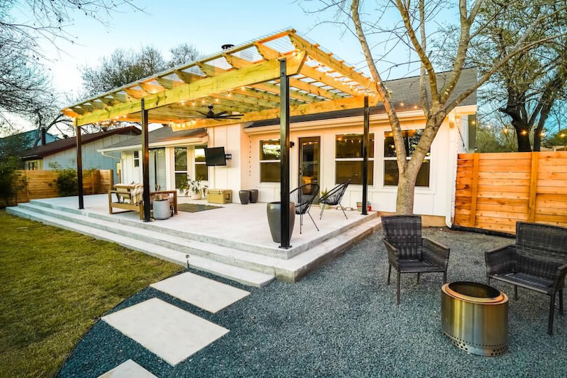 A patio with chairs and a sofa covered by a wooden pergola.