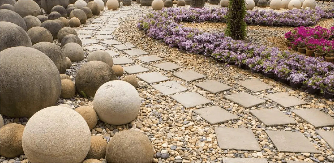 An stone path atop pebbles winding alongside purple flowers.