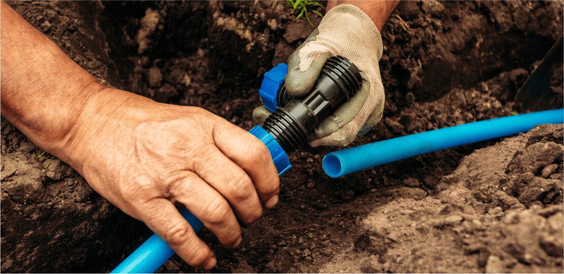 Hands installing a blue pipe in the ground.