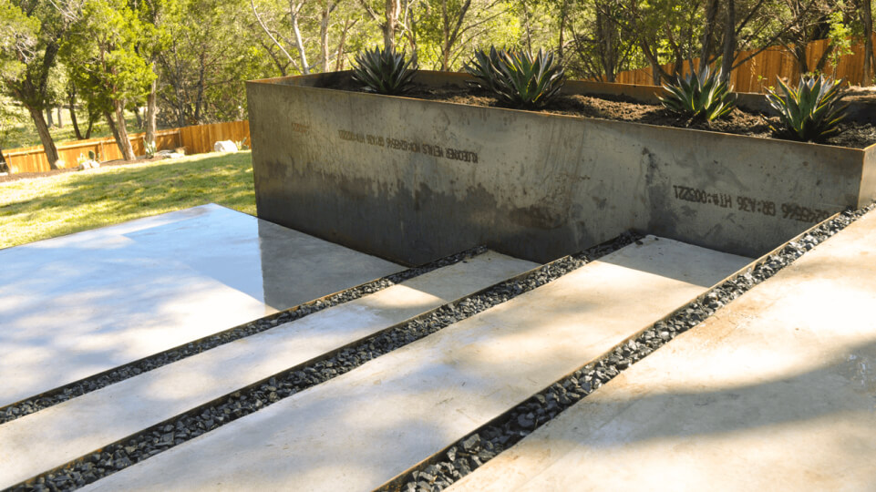 Concrete steps with a metal planter on the right side of them.