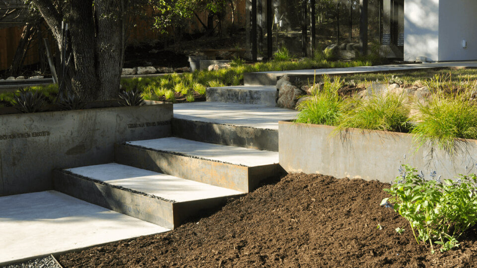 Concrete steps with metal planters and dirt along the sides of the steps.