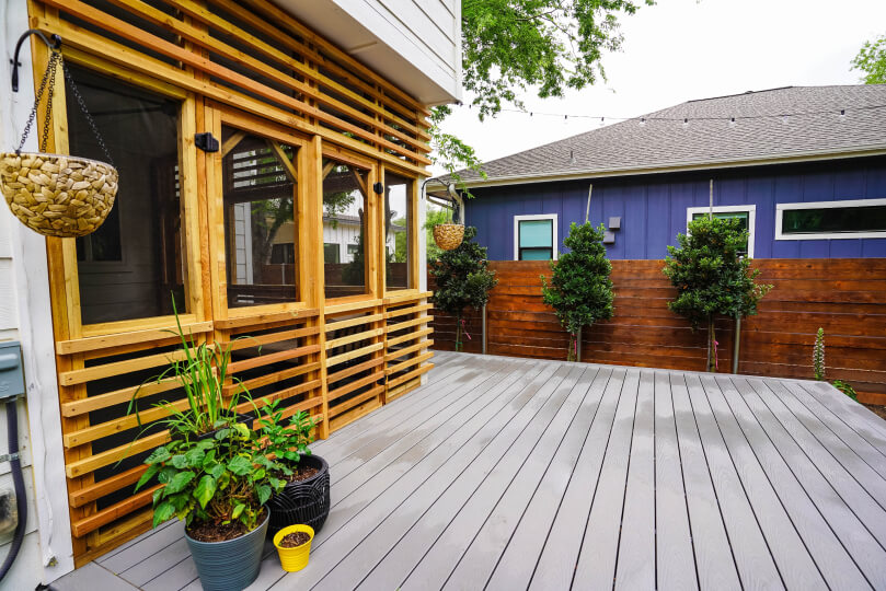 Grey deck with a screened in porch on top of it; there are light wooden slats around the edge of the porch.