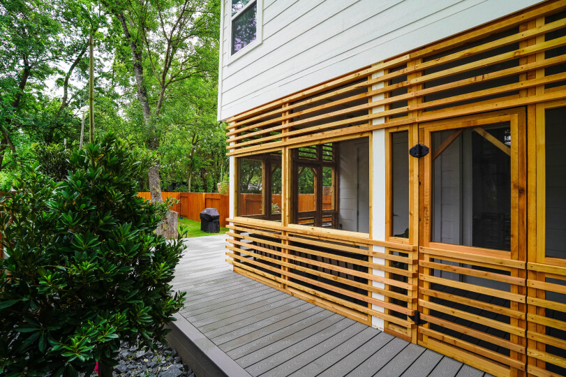 Trees next to a grey deck with a screened in porch with light wood slats around it.
