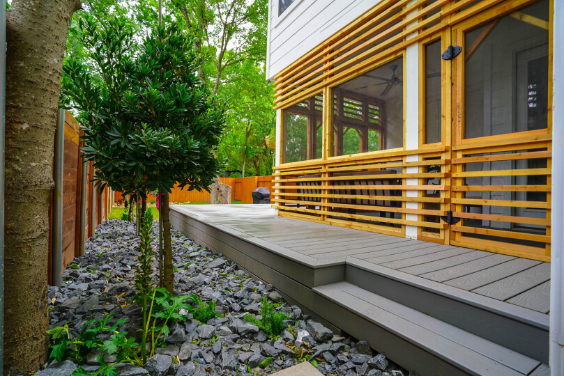 Trees next to a grey deck with a screened in porch with light wood slats around it.