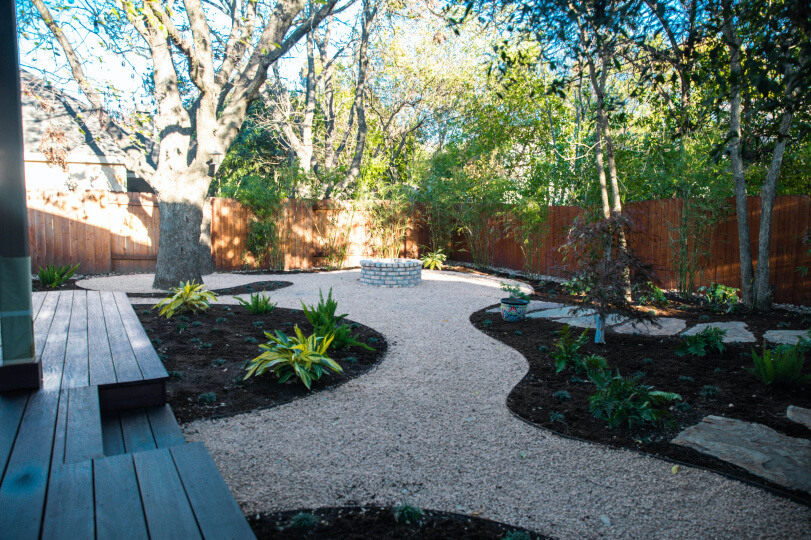Backyard with trees, gravel path, and areas of mulch with newly planted shrubs.