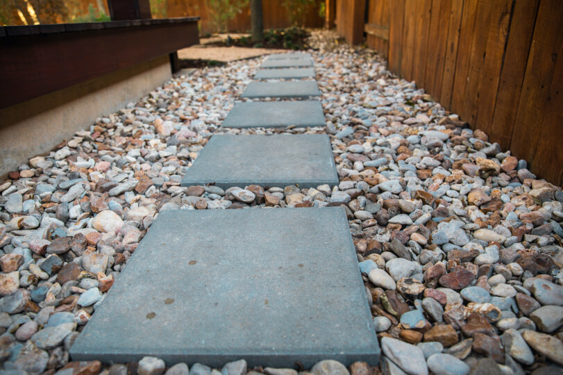 Square cement pavers laid in a path atop large pebbles.