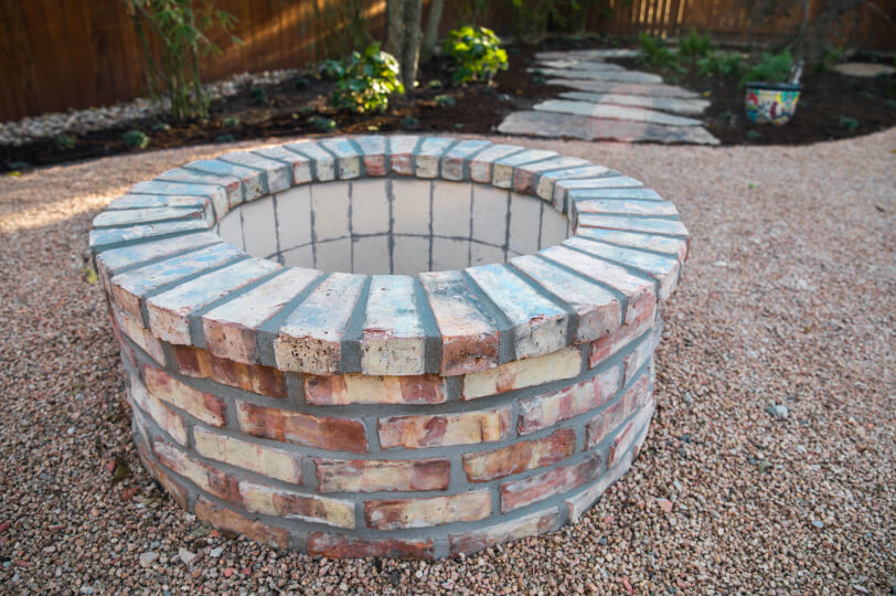 Red brick circular fire pit on top of gravel.