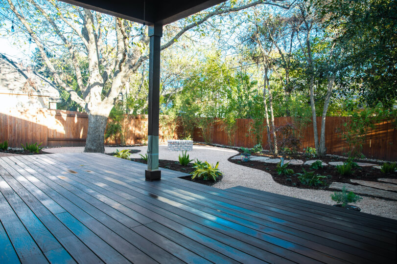 Dark wooden deck overlooking a backyard with areas of gravel, trees, and mulch.