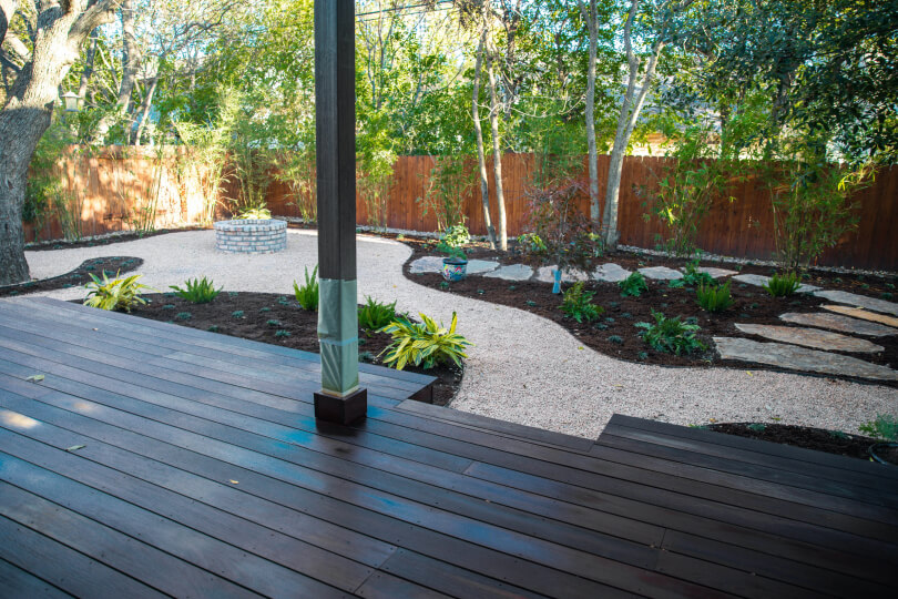 Dark wooden deck overlooking a backyard with areas of gravel, trees, and mulch.