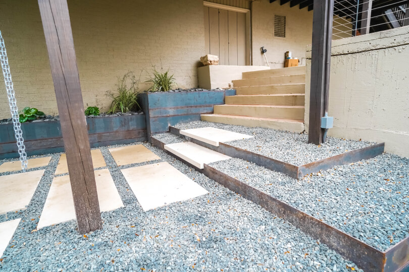 Lightly-colored rectangular pavers lined with grey pebbles in stepped levels leading to stairs.