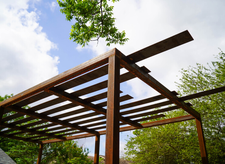 View of the top of a metal pergola, showing metal slats with gaps between them.