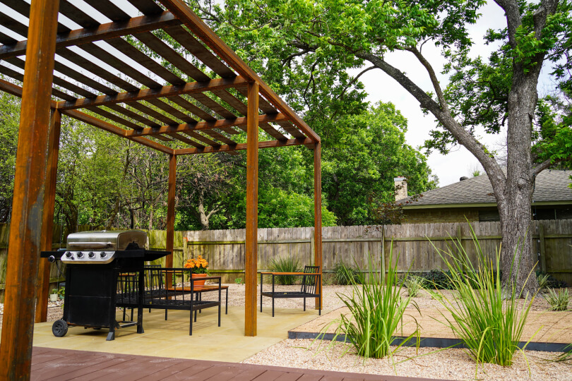 Metal pergola with a grill and outdoor tables and chairs underneath it.