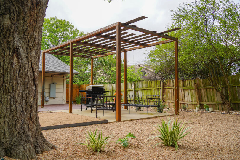 Metal pergola with a grill and outdoor benches underneath it.