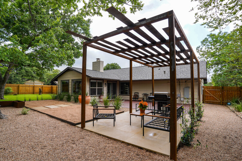Metal pergola with an outdoor seating area and a grill underneath it.
