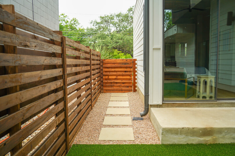 A wooden fence with horizontal slats and paved stone path.