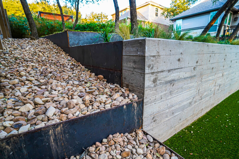 Close up of a corner of a cement planter with tiered levels filled with small rocks.