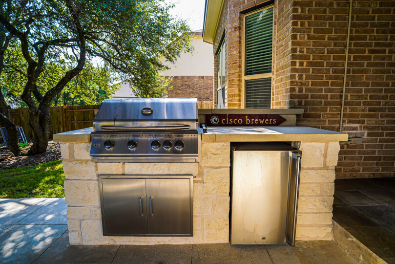 Stainless steel grill and mini fridge built into a light stone workspace.