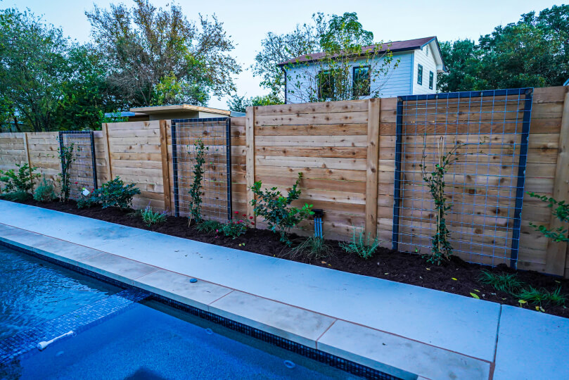 Close up of a light wooden fence with plants and trellises along the side.