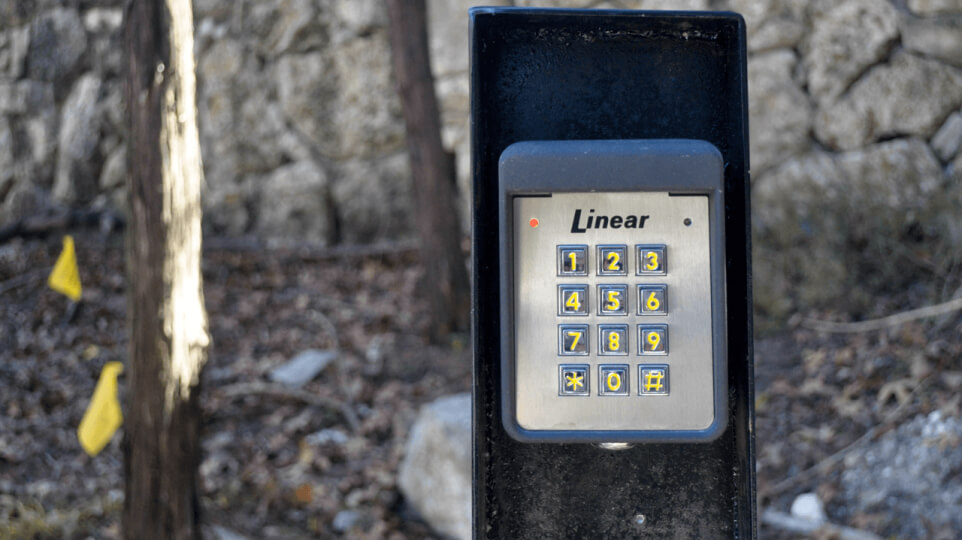 Close up of a keypad for a gate on a metal stand. Trees can be seen in the background.
