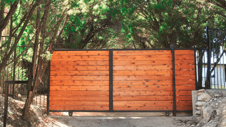 Stained wooden gate on wheels with metal framing. Trees can be seen behind the gate.