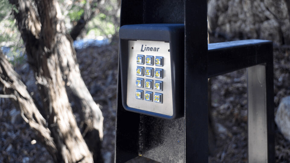 Gatecode keypad on a metal stand. Trees can be seen in the background.