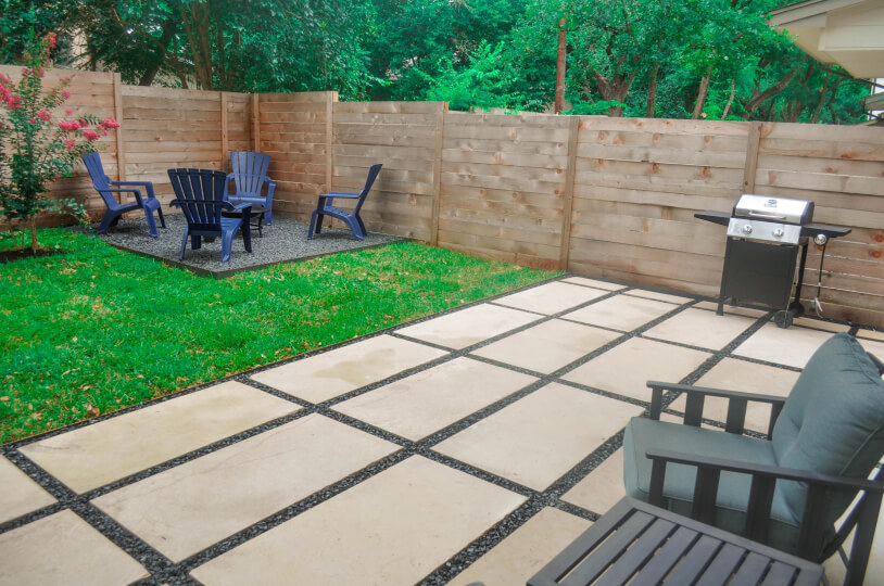 Wide view of a backyard with white rectangular stone landscaping. A grassy backyard and a fireplace are in the background.