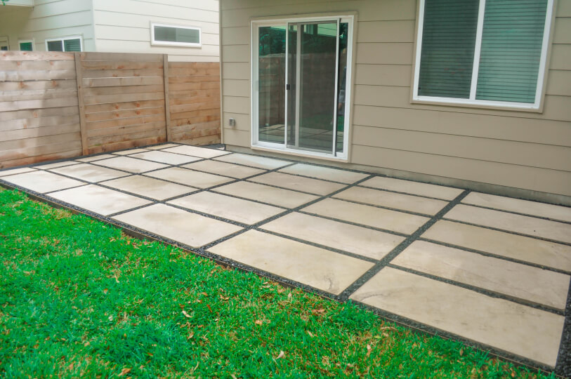 White rectangular stone patio connected to the back of the house with a sliding glass door.