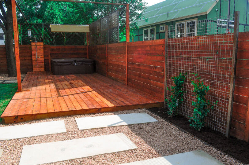 A wooden patio surrounded by a wooden fence. You can also see gravel with white stepping stones.