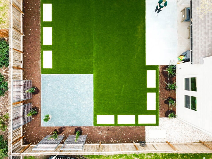 Top view of a house with a landscaped backyard. There is a grass section with white stepping stones going around it.