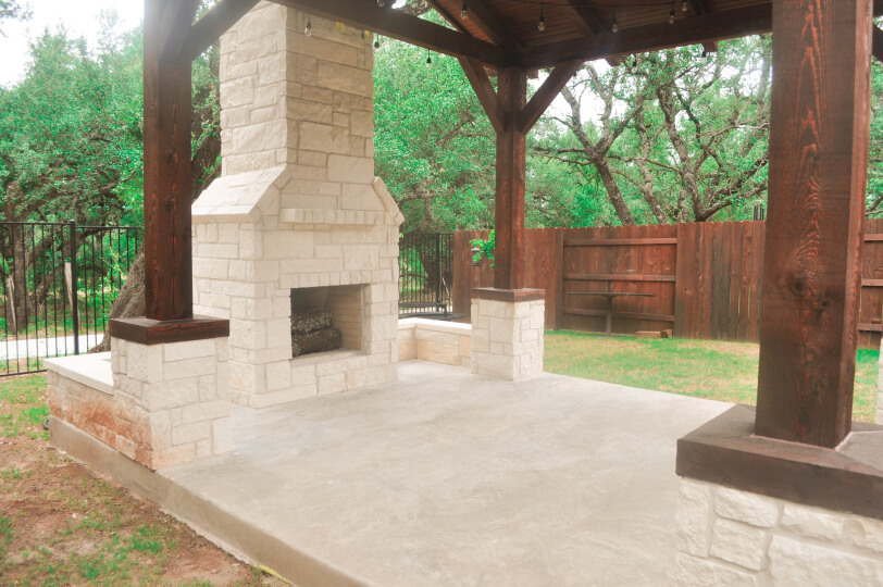 Side view of a stone fireplace under a covered patio in a backyard.